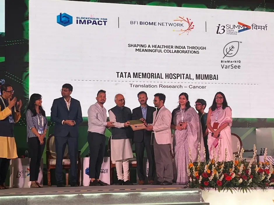 A handover on a Blockchain for Impact stage; the screen reads Tata Memorial Hospital, Mumbai, Translation Research – Cancer, beside the VarSee logo.