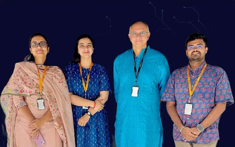 Four people wearing lanyards stand together against a dark background.