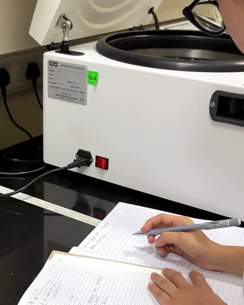 A team member writes in a lab notebook beside a centrifuge.
