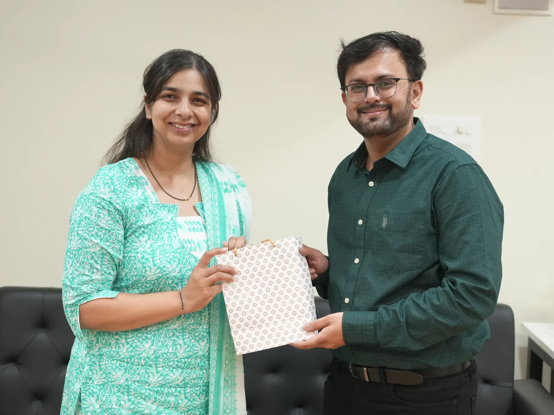 Manasi Khasnis and a collaborator hold a gift bag together in an office.