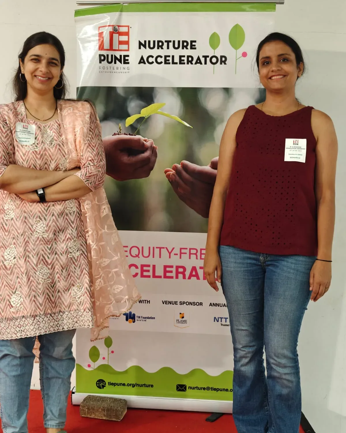 Manasi Khasnis and Snahlata Singh beside a TiE Pune Nurture Accelerator standee.
